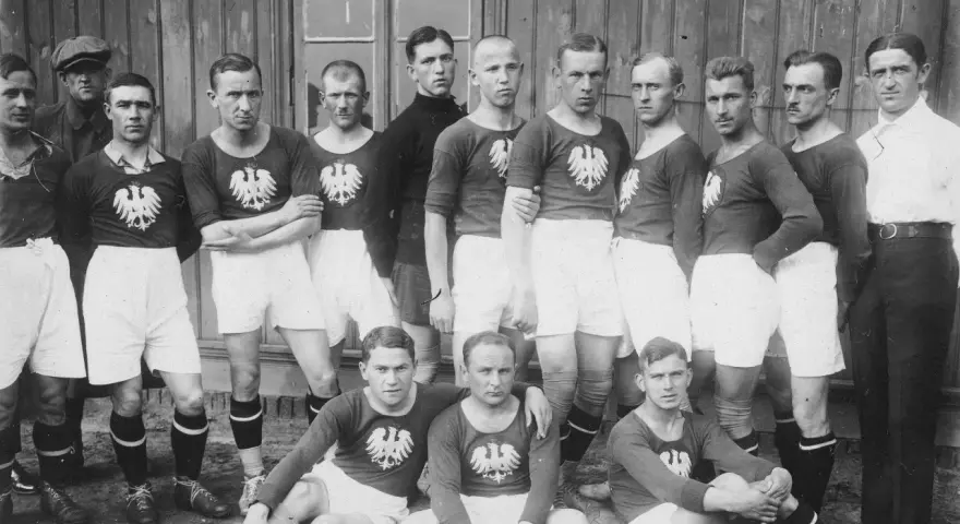 Drużyna piłkarska pozuje do zdjęcia. Widać, ile osób gra w piłkę nożną: 15 zawodników w strojach z orłem.