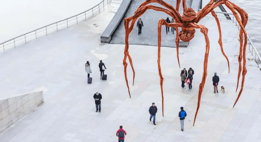 Une immense araignée de bronze, œuvre de Louise Bourgeois, domine une place où quelques passants curieux l'observent.