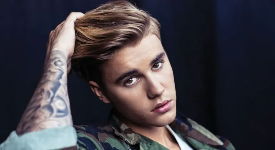 Justin Bieber mit tätowiertem Arm und Camouflage-Jacke, blickt in die Kamera.
