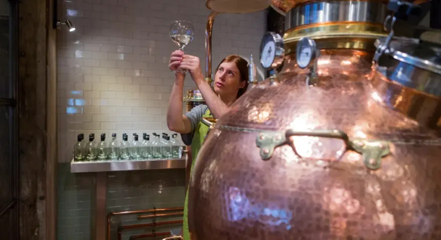 Frau prüft mit einem Glas die Qualität des Destillats. Dies ist ein Schritt, wie wird Gin hergestellt, in einer Kupferbrennerei.