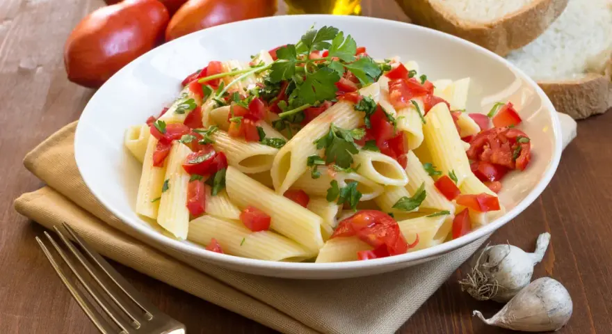 Świeży makaron penne z pomidorami i pietruszką, obok chleb, czosnek i oliwa. Porównanie makaronu świeżego z lodówki kontra suchego z paczki.