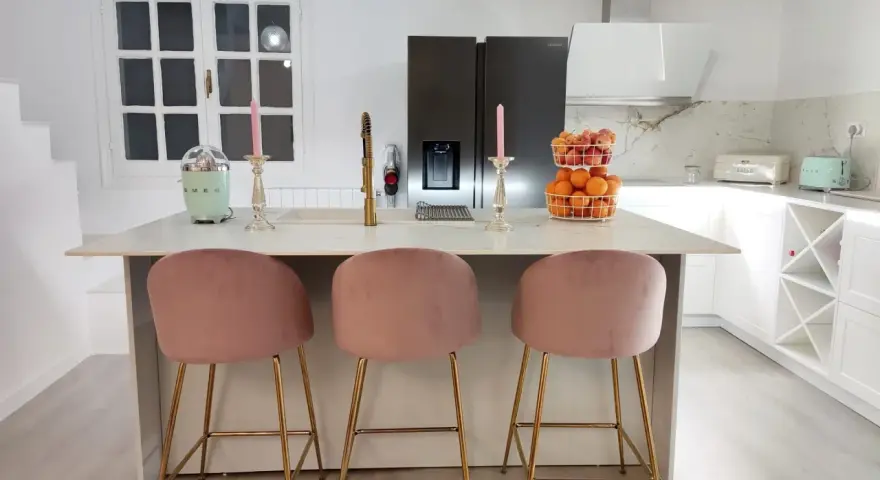 Elegantes cocinas con isla, tres taburetes rosas y dorados invitan a disfrutar.
