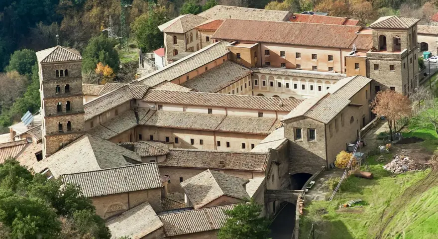 Aerial view of a sprawling monastery complex near Rome, with terracotta roofs and a tall bell tower.