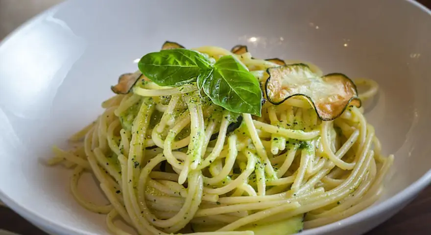 Spaghetti cremosos con calabacín y albahaca en un cuenco blanco.