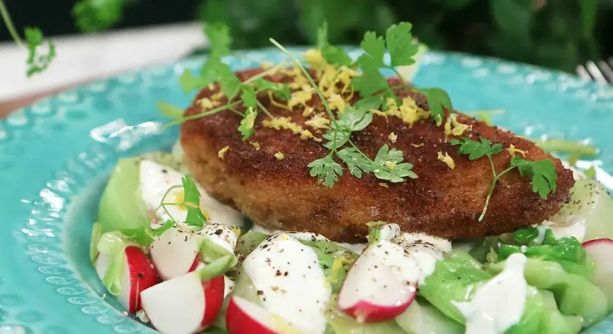 En gyllene kyckling kiev toppas med citronzest och persilja, serverad på en bädd av krispig sallad med rädisor och krämig dressing.