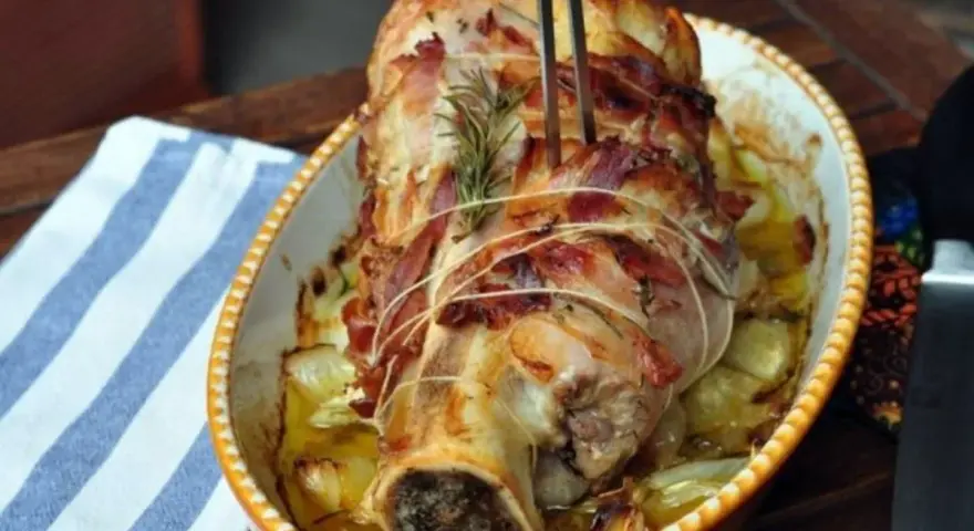Stinco di vitello al forno, avvolto in pancetta e cotto con cipolle e rosmarino, pronto per essere servito.