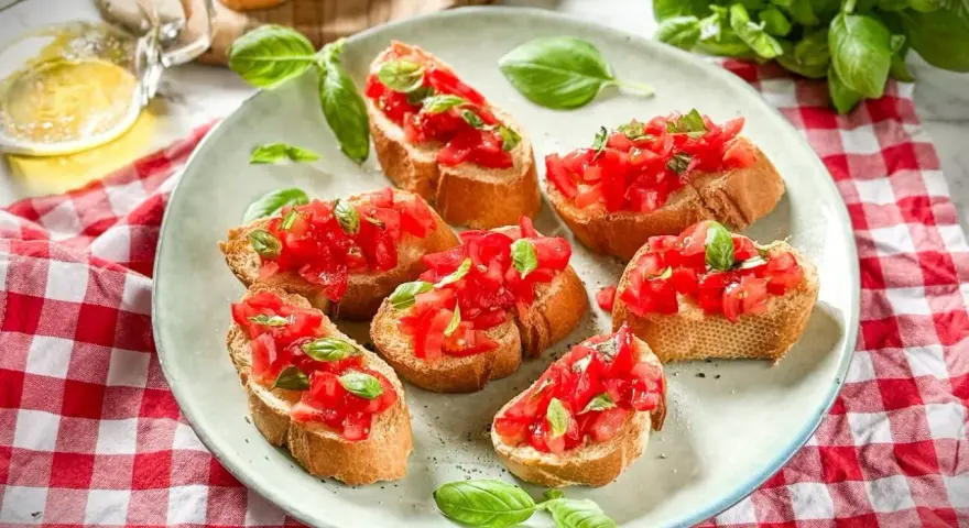 Frische Crostini Variationen mit Tomaten und Basilikum auf einem Teller, garniert mit frischen Basilikumblättern.