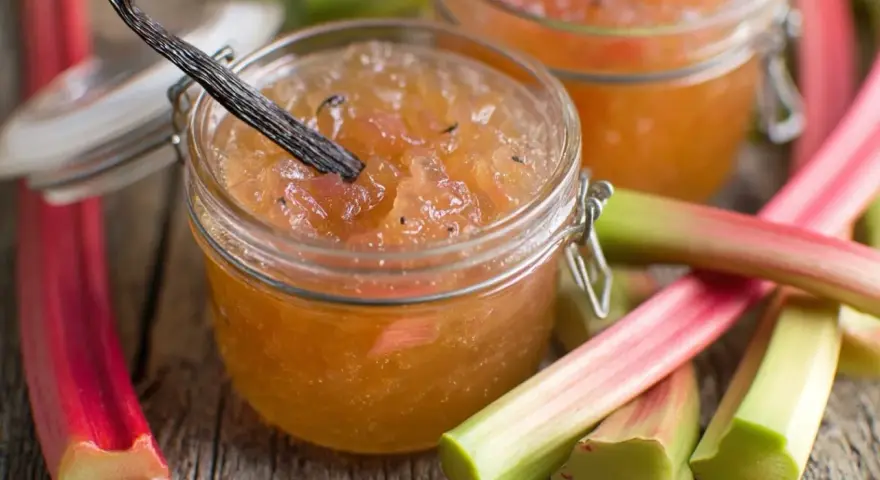 Confiture de rhubarbe maison, avec une gousse de vanille, sur un fond de tiges de rhubarbe fraîches.