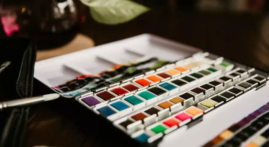 Une palette de matériel peinture aquarelle aux couleurs vives, prête à l'emploi. Un pinceau est posé à côté.
