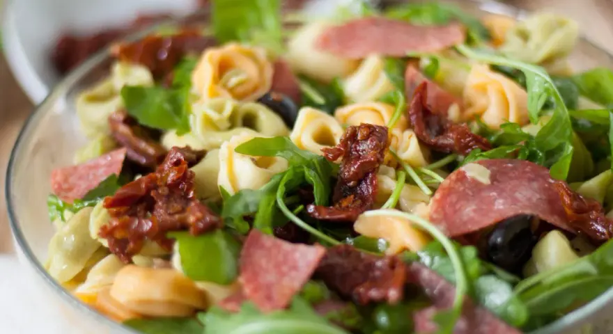 Kolorowa sałatka z tortellini, rukolą, suszonymi pomidorami i salami. Idealna na letni obiad.