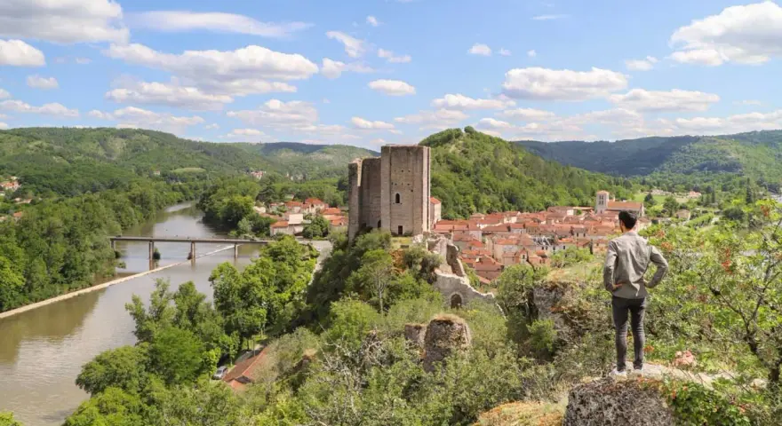 Un homme admire un village médiéval avec un château, un fleuve et des collines verdoyantes, un aperçu du circuit des plus beaux villages du Lot.