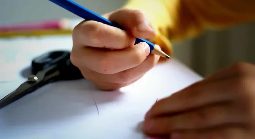 Dziecko pisze wzruszający list do taty. Na stole leżą nożyczki i kredki.
