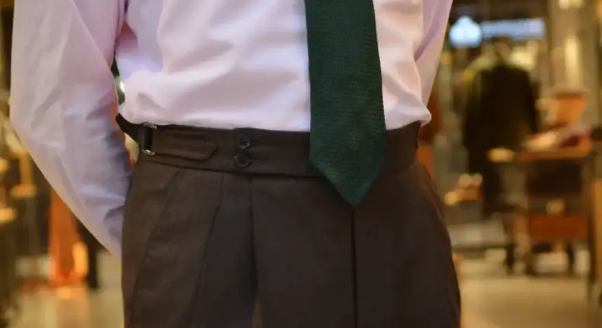 Elegancki mężczyzna w różowej koszuli i brązowych spodniach. Zielony krawat sięga idealnie do klamry paska.