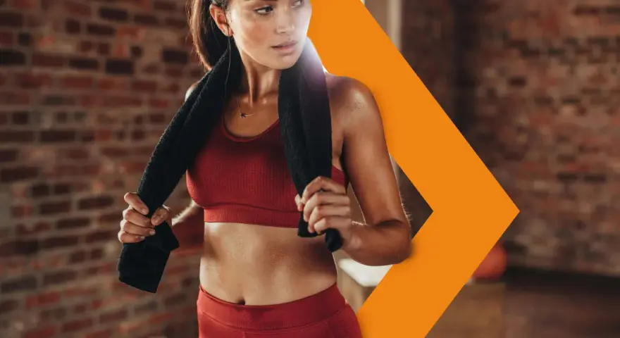 Donna sudata in abbigliamento sportivo rosso, con un asciugamano nero, si riposa dopo l'allenamento. Con il caldo i battiti aumentano, ma lei è determinata.