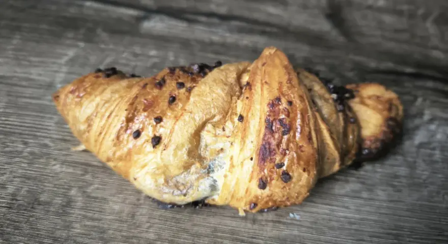 Chrupiący croissant z kawałkami czekolady na drewnianym tle. Idealny na śniadanie, choć warto sprawdzić jego kcal.