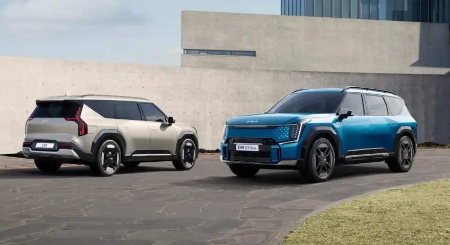Dwa samochody elektryczne Kia EV9 w kolorach niebieskim i jasnoszarym stoją na zewnątrz.