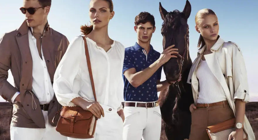 Quattro modelli con un cavallo, vestiti in stile old money, evocano un'eleganza senza tempo in un paesaggio aperto.