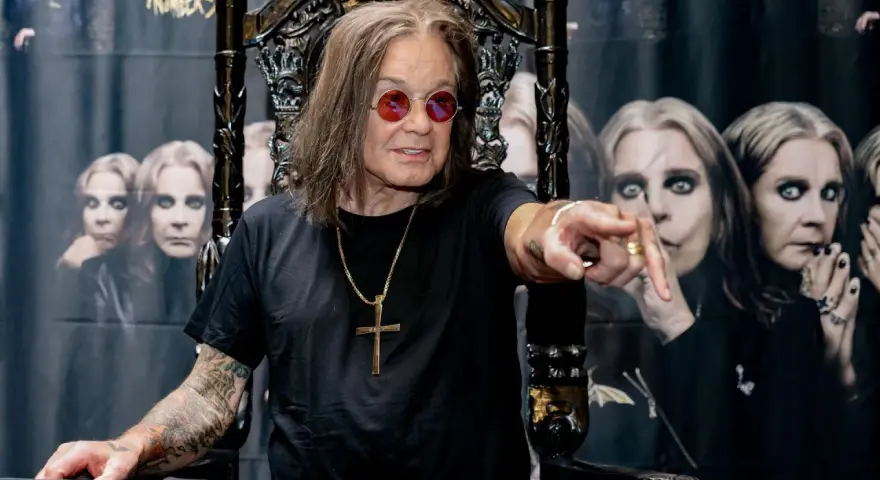 Ozzy Osbourne, geboren 1948, sitzt auf einem Thron und zeigt mit dem Finger. Im Hintergrund sind Bilder von ihm zu sehen.
