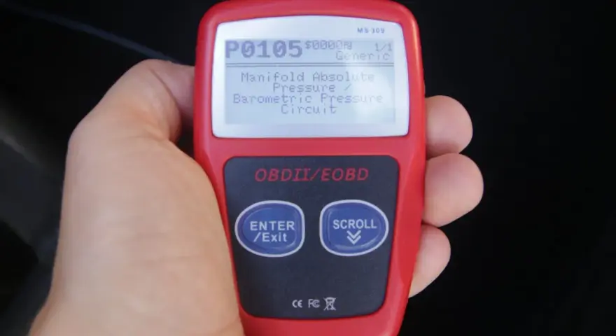 Ręka trzyma czytnik OBD, wyświetlający kod błędu P0105: "Manifold Absolute Pressure / Barometric Pressure Circuit". To jeden z wielu kodów błędów OBD po polsku.