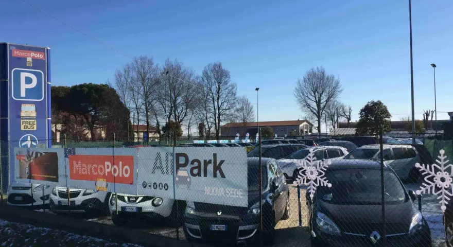 Parcheggio Marco Polo, con bus navetta gratuito per l'aeroporto. Auto parcheggiate dietro una recinzione con decorazioni a fiocco di neve.
