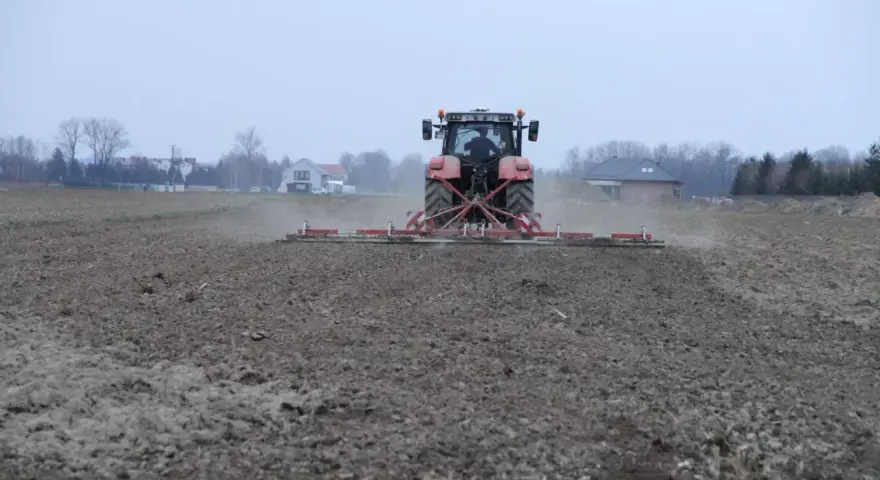 Czerwony traktor z agregatem uprawowym przygotowuje pole pod zasiew. Dzierżawa ziemi w pełni.