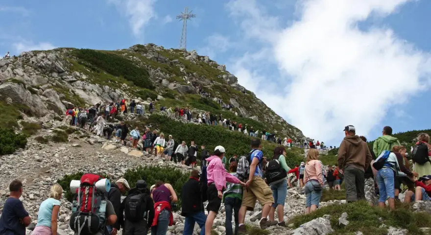 Tłum turystów wspina się na Giewont, podziwiając widok z Kasprowego Wierchu. Na szczycie widoczny krzyż.