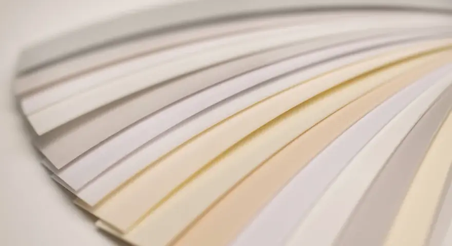 Próbki papieru ułożone wachlarzowo, ukazujące subtelne odcienie bieli i beżu.