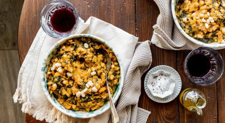 Un piatto di fagioli e verdure, un classico esempio di cose tipiche toscane, accompagnato da vino rosso e olio.