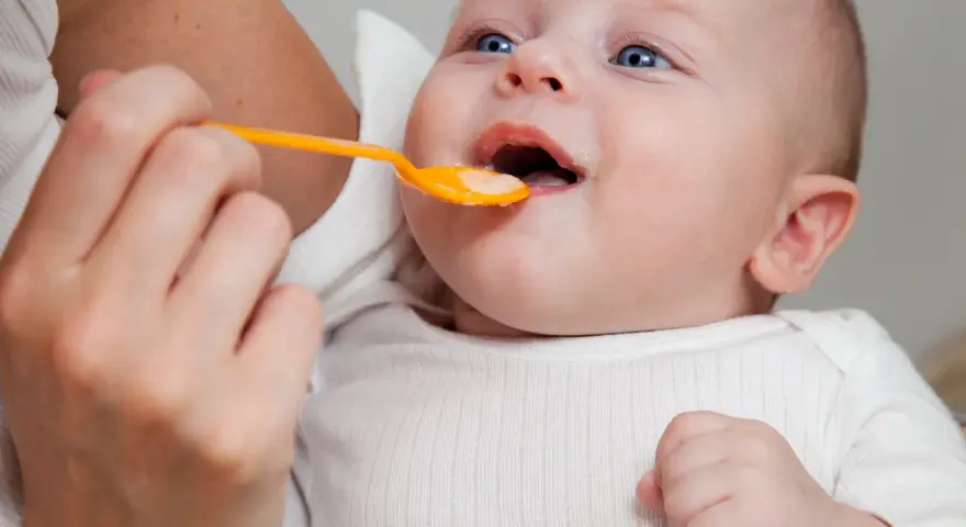 Rączka podaje łyżeczkę z jedzeniem, co dla 6 miesięcznego dziecka jest nowym doświadczeniem.