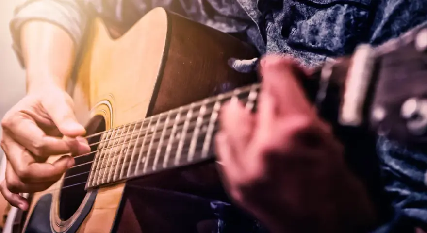 Dłonie grające na gitarze akustycznej. Czy gra na gitarze jest trudna? Zależy od determinacji i praktyki.