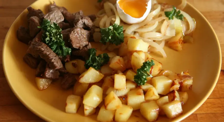 En tallrik med stekt kött, stekt potatis, stekt lök och ett kokt ägg. En klassisk rätt som representerar svenskt mat.