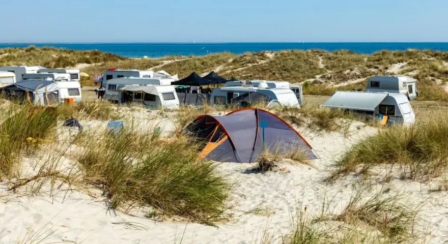 Ein sonniger Campingplatz in Deutschland am Meer. Wohnwagen und Zelte stehen zwischen Dünen und Strandhafer.
