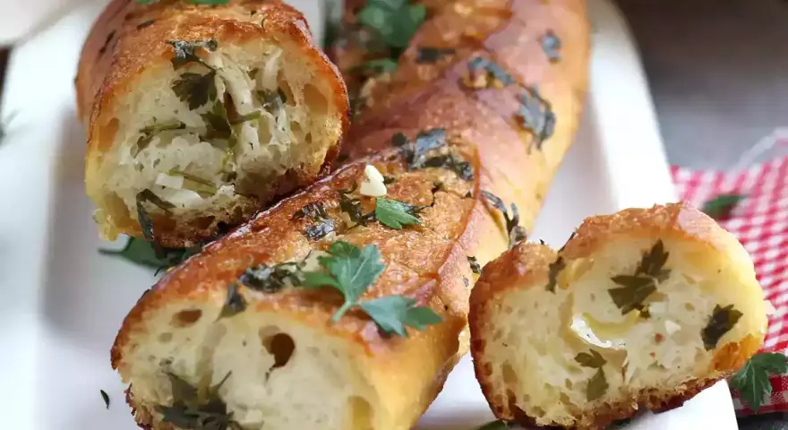 Pan de ajo recién horneado, dorado y crujiente, con trozos de perejil y ajo visibles en su interior.