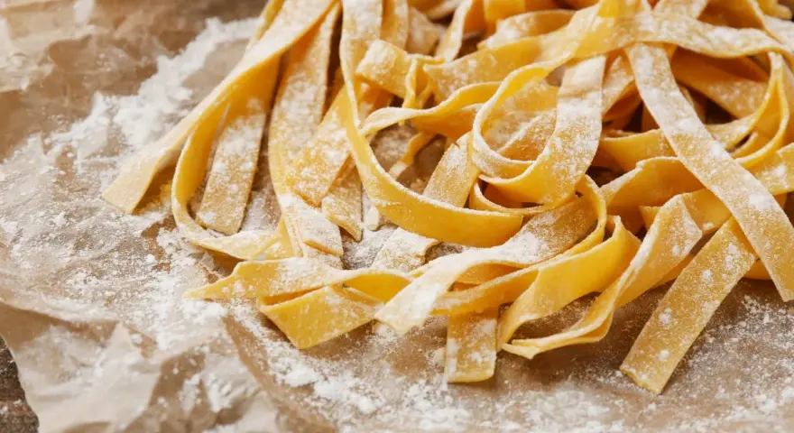 Świeży, domowy makaron tagliatelle, posypany mąką, czeka na gotowanie. Idealny przepis, jak zrobić makaron.