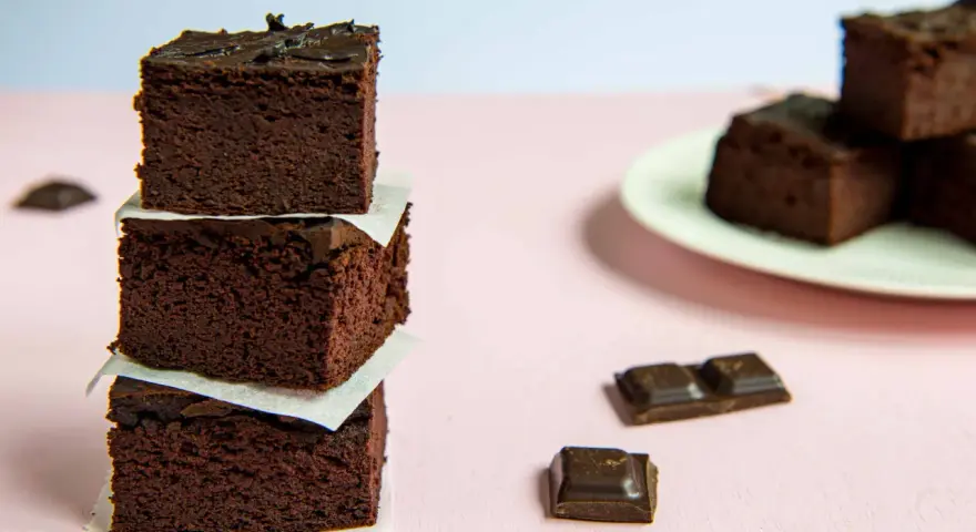 Ciemne, wilgotne brownie z fasoli i bananów, ułożone w wieżę, obok kawałków czekolady.