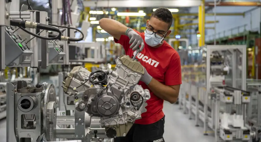 Operaio con mascherina e guanti lavora su un motore Ducati in fabbrica. Un'emozione da museo.