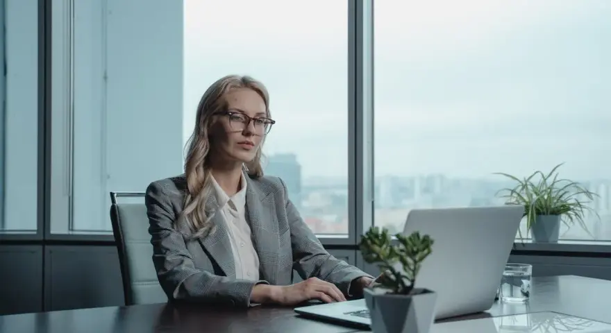 Kobieta w okularach pracuje przy laptopie, przygotowując list motywacyjny na stanowisko kierownicze. Wzór dokumentu jest kluczowy.