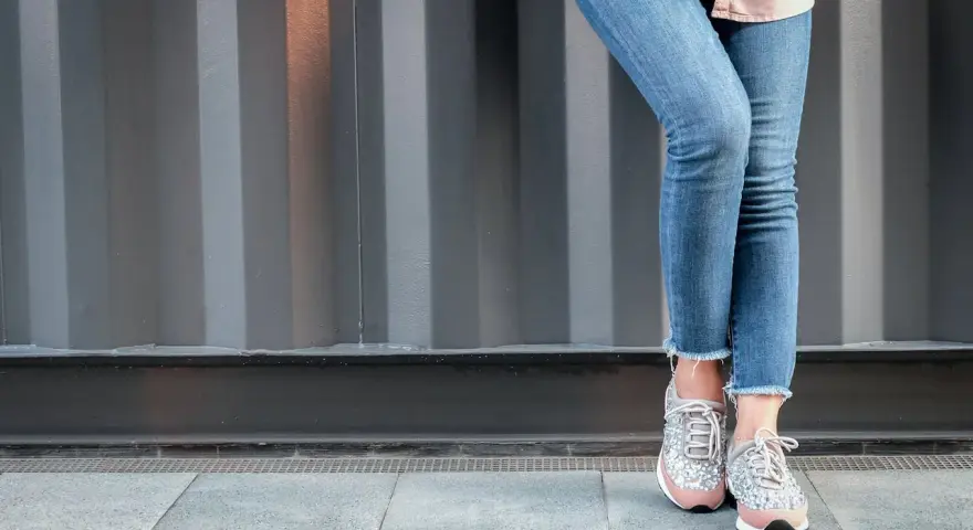 Nogawki jeansów postrzępione na dole, w połączeniu z błyszczącymi sneakersami, tworzą modny look.