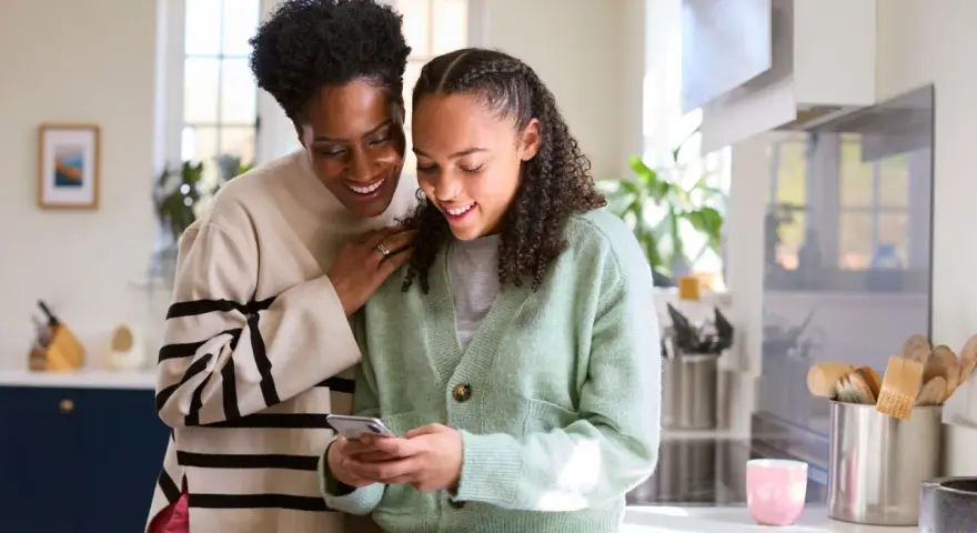 Mère et fille souriantes regardant un téléphone. Une conversation sur la pension alimentaire jusqu'à quel âge.