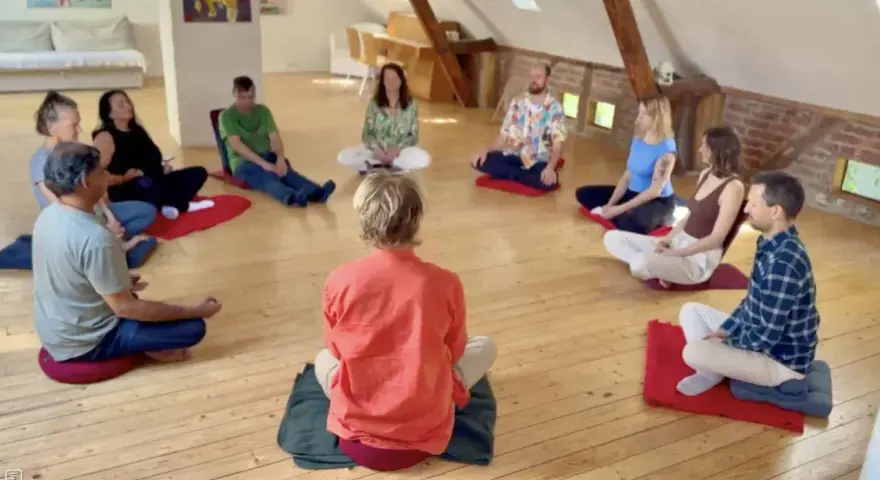 Menschen sitzen im Kreis auf Meditationskissen. Eine Gruppe genießt eine **Auszeit im Kloster**, umgeben von Ruhe und Gemeinschaft.