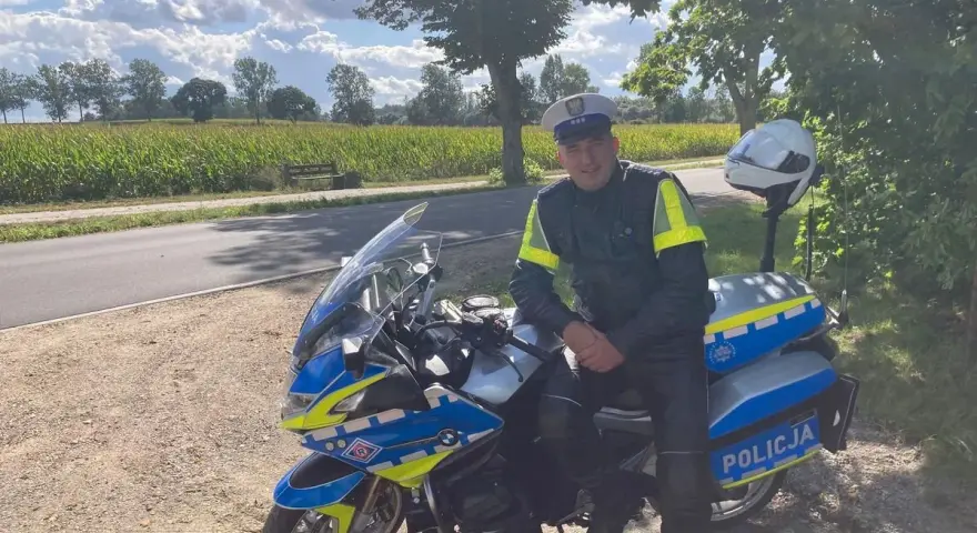 Policjant w pełnym umundurowaniu siedzi na swoim policyjnym motocyklu, gotowy do służby.