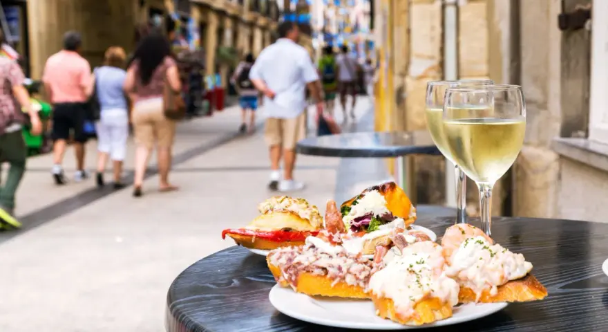 Njut av utsökt san sebastian mat och vitt vin på ett café. Folk promenerar på gatan i bakgrunden.