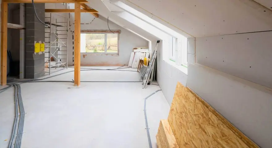 Wnętrze domu w trakcie budowy, widoczne materiały budowlane, instalacje i rusztowanie.