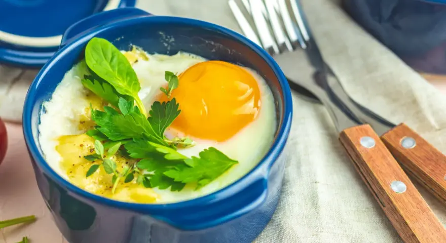 Un œuf cocotte appétissant dans un ramequin bleu, garni d'herbes fraîches. Un délice pour le petit-déjeuner.