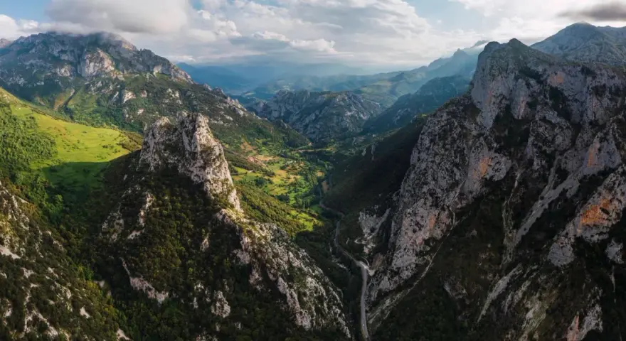 Majestätische Berge der Picos de Europa, grüne Täler und eine Straße, die sich durch die zerklüftete Landschaft schlängelt.
