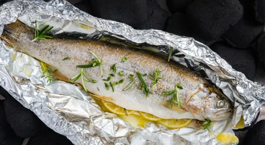 Eine ganze Forelle vom Grill in Alufolie, mit Zitronenscheiben und Rosmarin verfeinert, bereit für den Genuss.