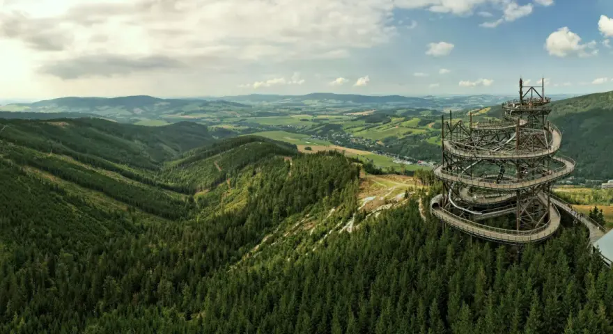 Widok na Sky Walk Czechy, spiralną wieżę widokową pośród zielonych wzgórz i lasów.