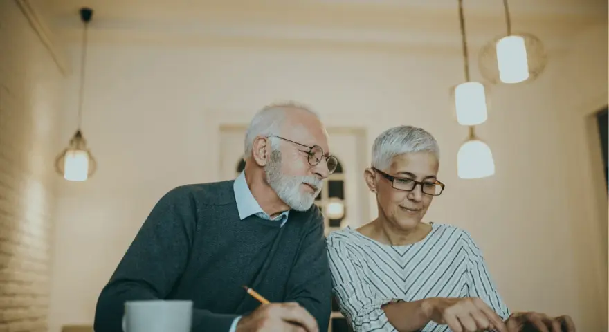 Couple âgé discutant de la différence entre article 82 et 83, l'un écrit, l'autre utilise une calculatrice.