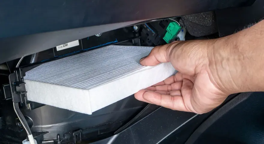 A hand removes a new cabin air filter from its packaging, ready to install it. This shows how to change cabin air filter for cleaner air.