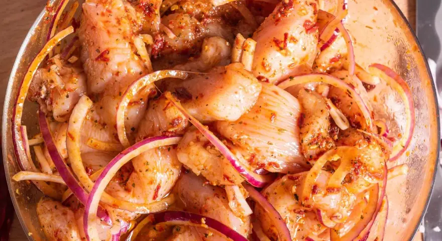 Kawałki kurczaka w misce z czerwoną cebulą i przyprawami, gotowe na grill. Pyszna marynata do kurczaka na grilla.